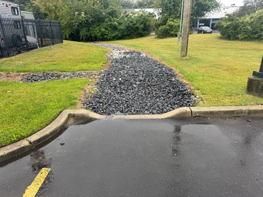 Fixed parking lot drainage swale in Toms River, NJ with new rip rap stone and geotextile fabric preventing pooling and icing
