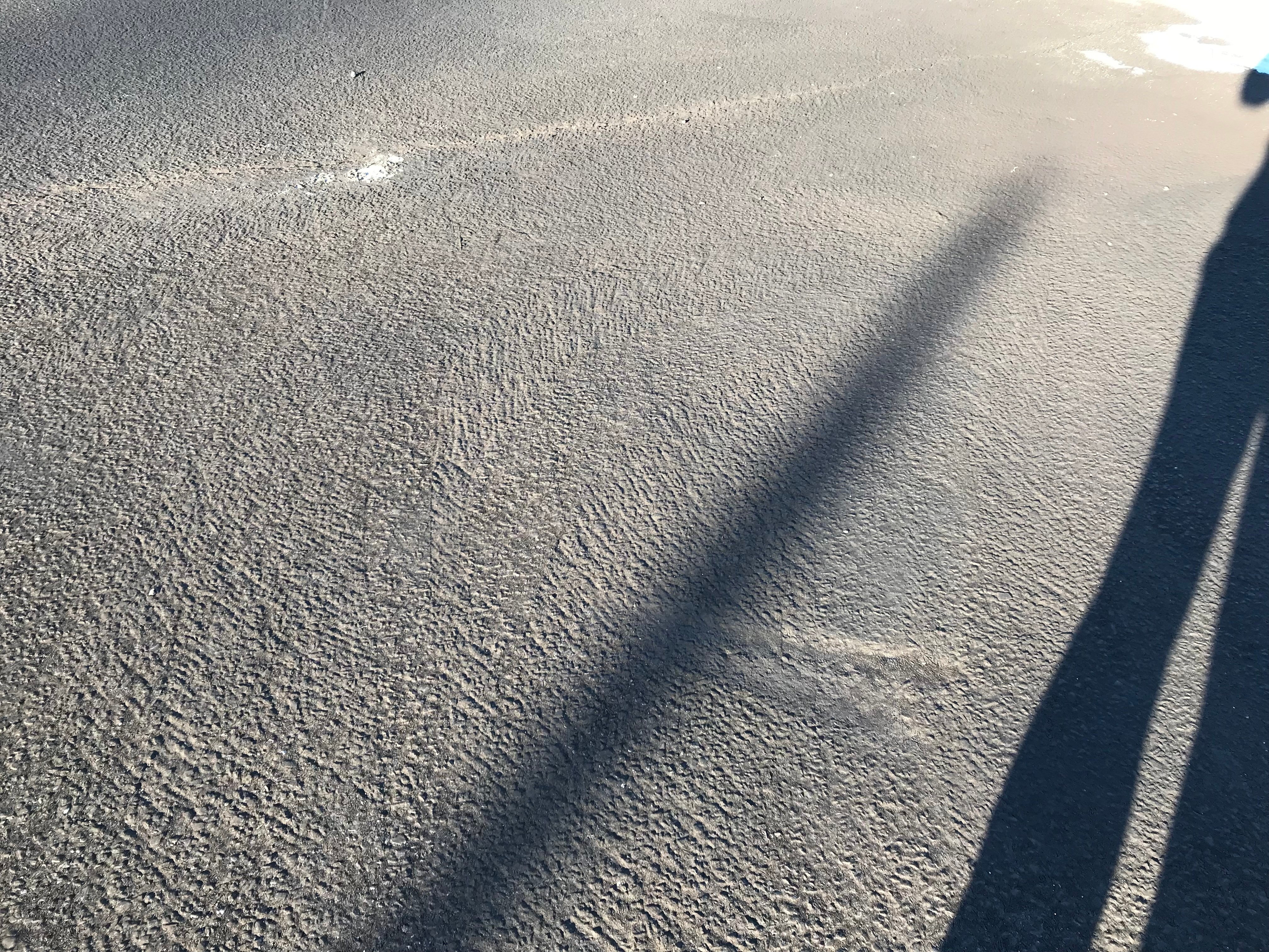 Failed pavement sealer showing grey, patchy areas caused by freezing temperatures after late-season application.