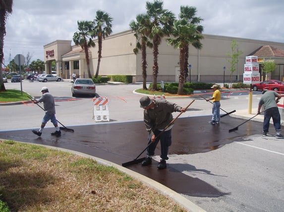 Crew applying asphalt sealcoat to a commercial parking lot in Jupiter, FL to protect pavement from sun, rain, and daily traffic wear.